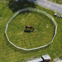 A circular wooden fence in a grassy field with a red vehicle parked nearby.