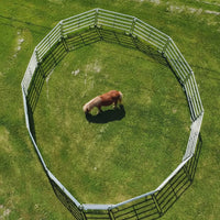 Circular wooden fence on a grassy field with rocks and a sign in the background.